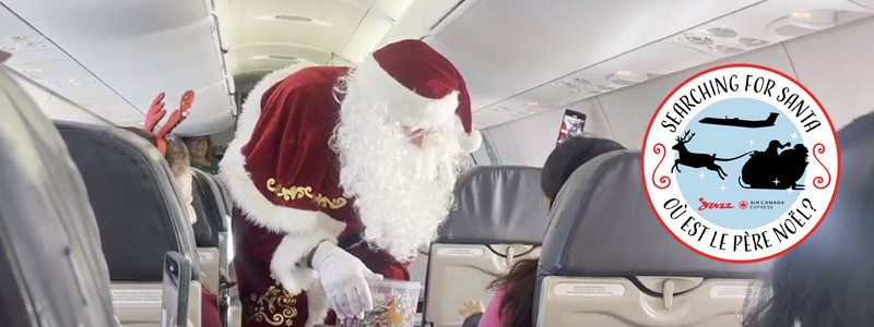 Santa Claus interacting with passengers on an airplane during the 'Searching for Santa' event, featuring logos of Air Canada Express and Jazz Aviation.