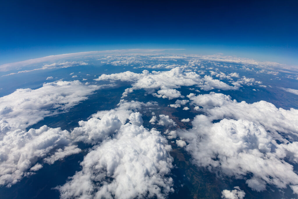 Aerial view of scattered clouds over varied terrain, including mountains and flatlands, taken from high altitude.